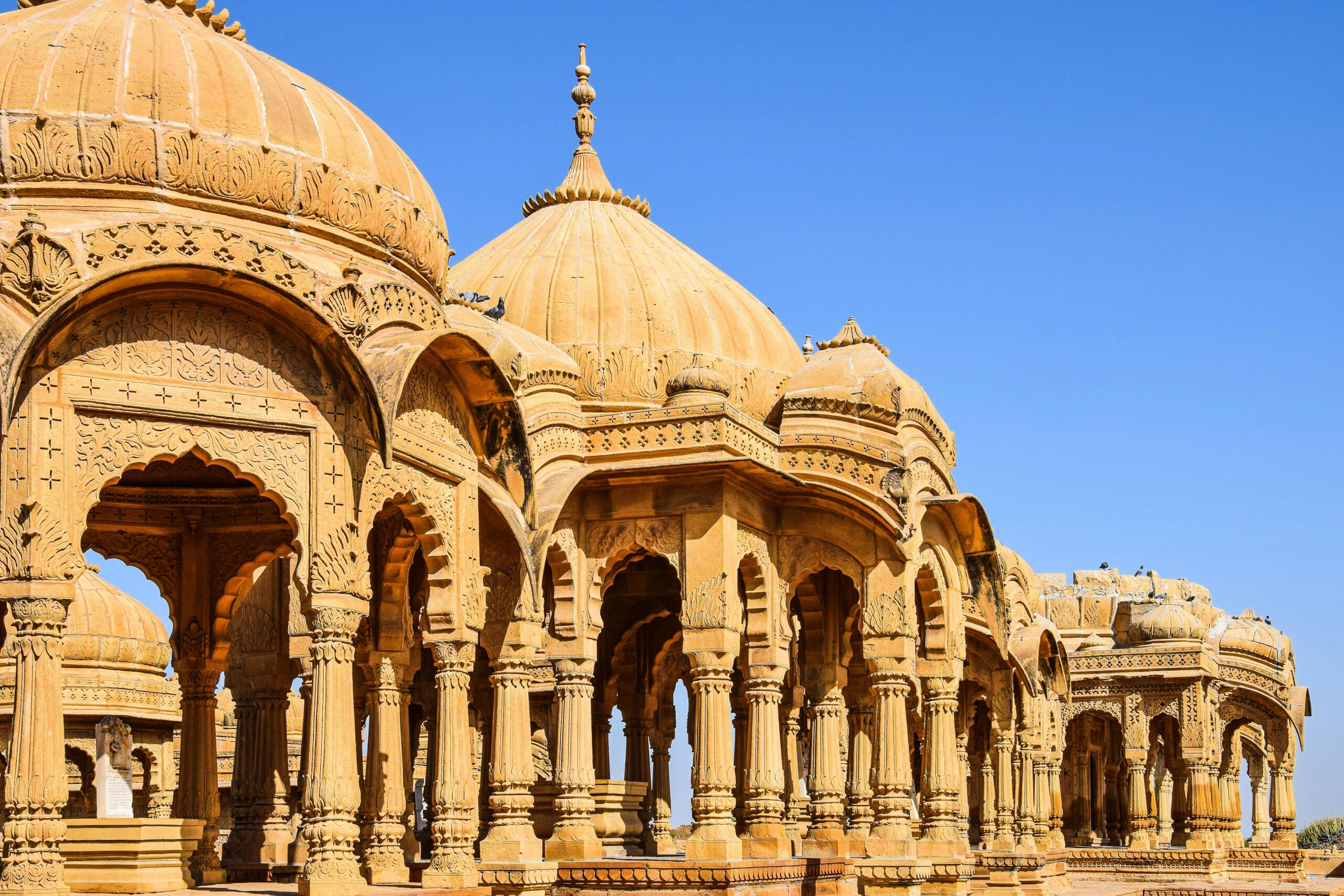 Historic stone temples with intricate domes under clear blue sky in Rajasthan, India.
