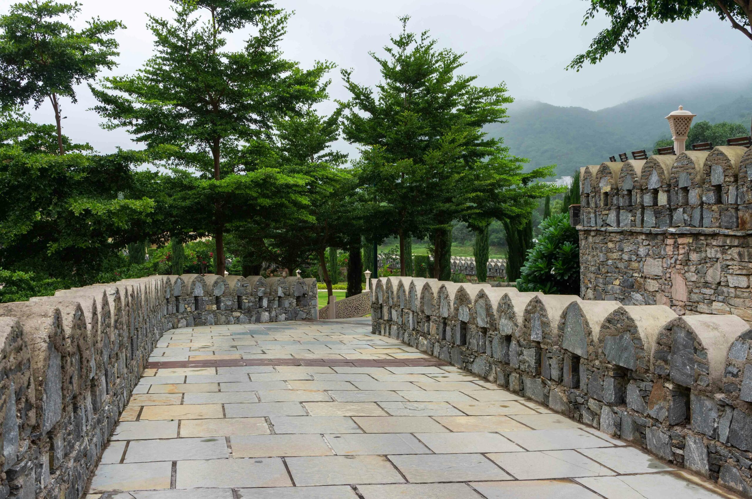 Explore the historic stone pathway leading to Kumbhalgarh Fort's lush greenery.